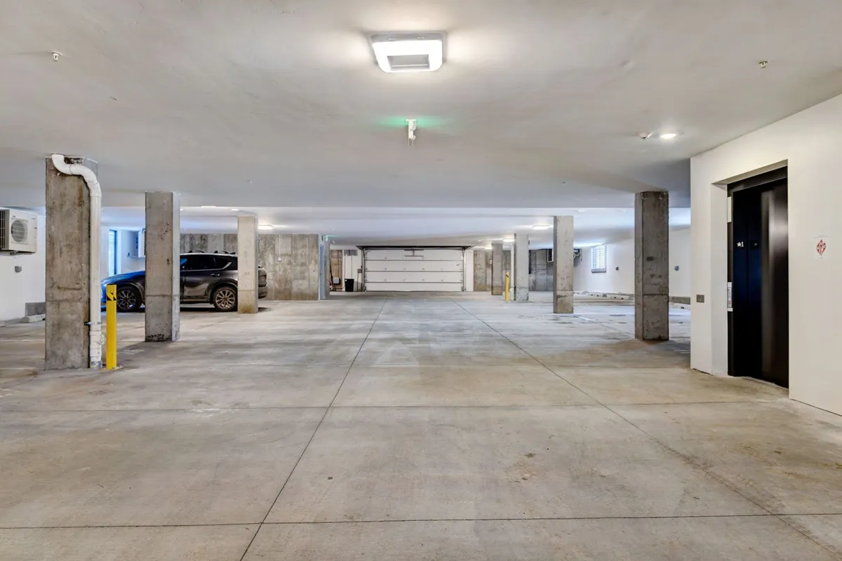 A tidy, well-lit interior parking garage with concrete pillars, an elevator entrance, and a parked car, illustrating secure and convenient vehicle storage.