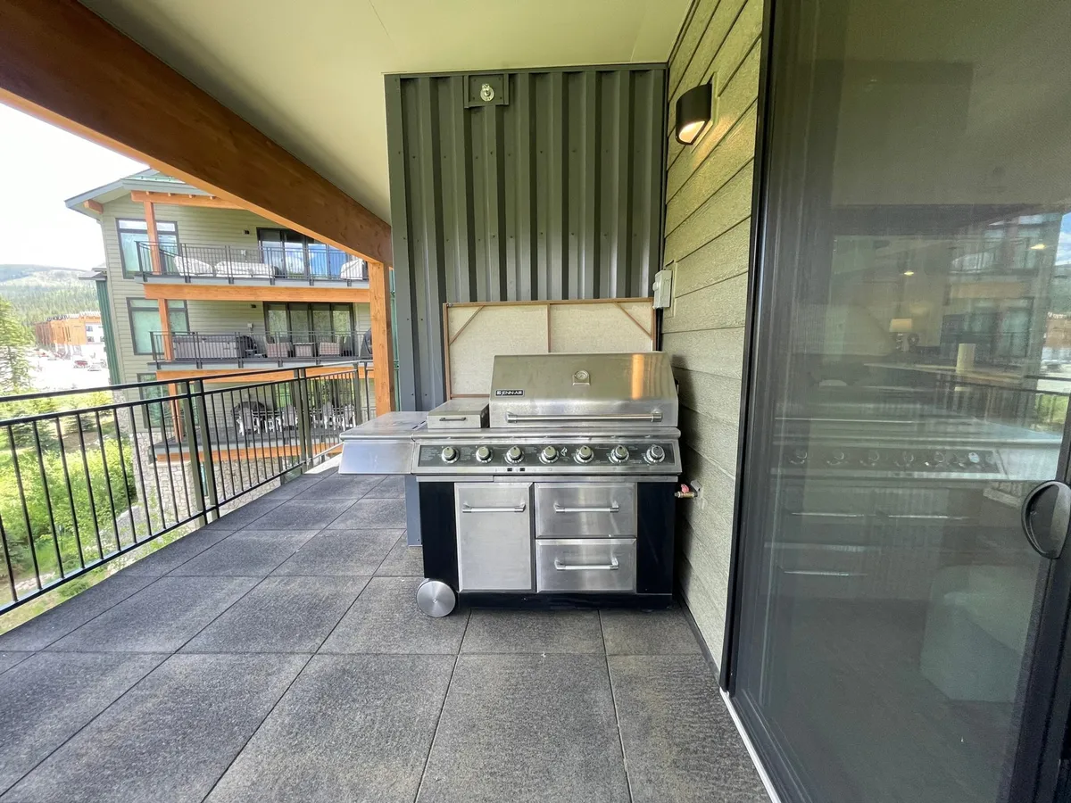 A balcony with a BBQ grill and railing overlooking the surrounding area. The setup is casual and functional, ideal for outdoor cooking and dining while enjoying views of the landscape.