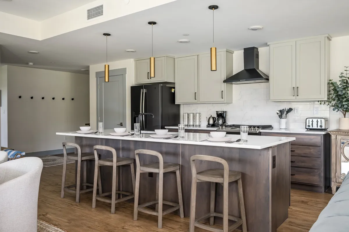 A modern kitchen with a central island and bar stools, surrounded by chic cabinetry and stylish lighting. The layout is designed for both cooking and entertaining, encouraging guests to gather and mingle while meals are prepared.