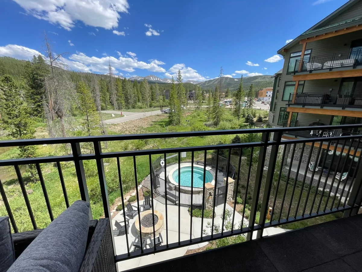 A serene view from a private balcony with comfortable seating and a bubbling hot tub, overlooking forested mountains and trees. The scene invites relaxation after an active day, with opportunities for stargazing or enjoying coffee with a view.