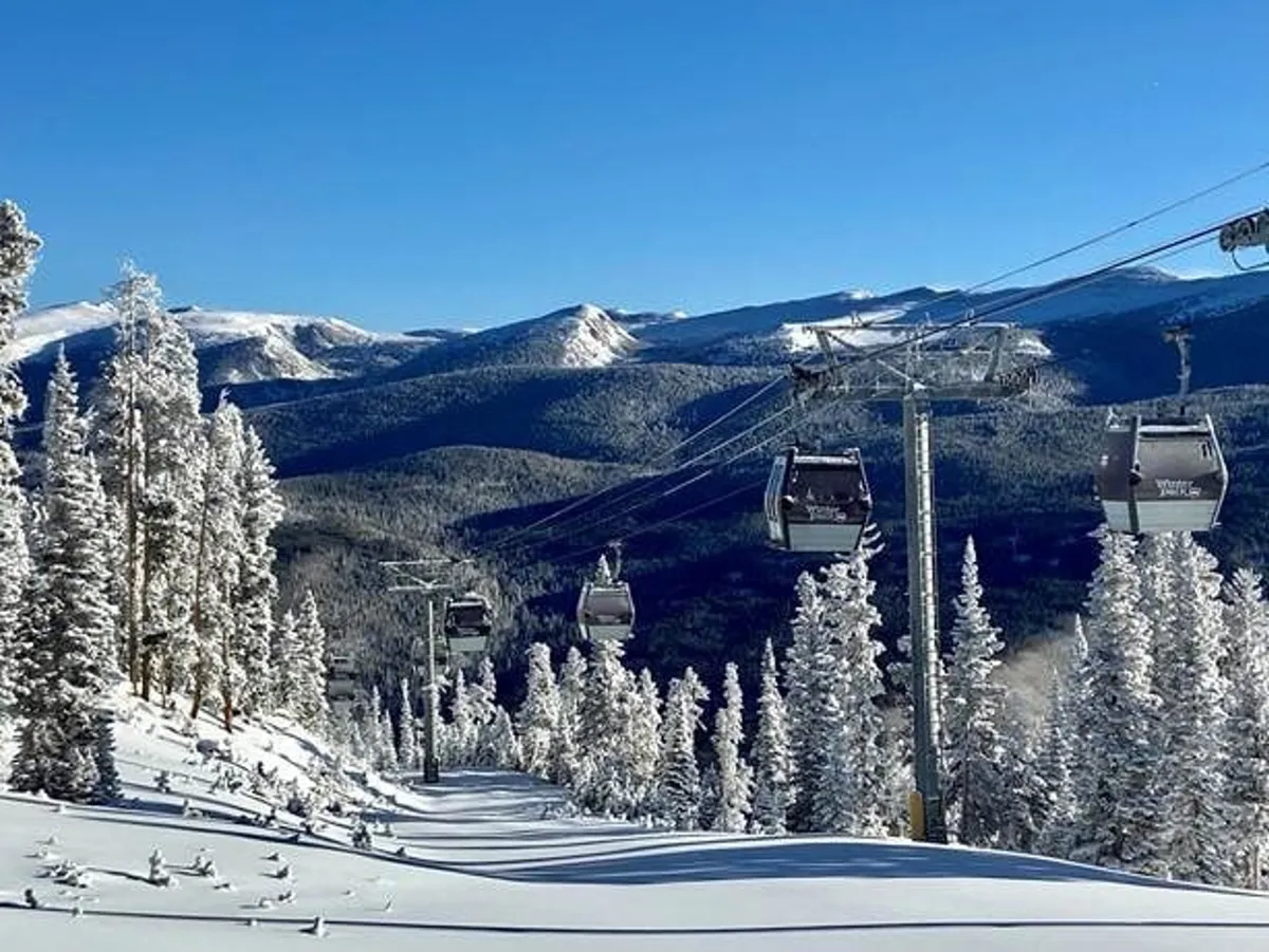 A panoramic view of ski lift gondolas gliding over a snow-covered mountain landscape, with majestic mountain ranges in the background. The open area below features skiers and snowboarders, evoking the sense of adventure and alpine excitement that typifies a world-class ski resort.