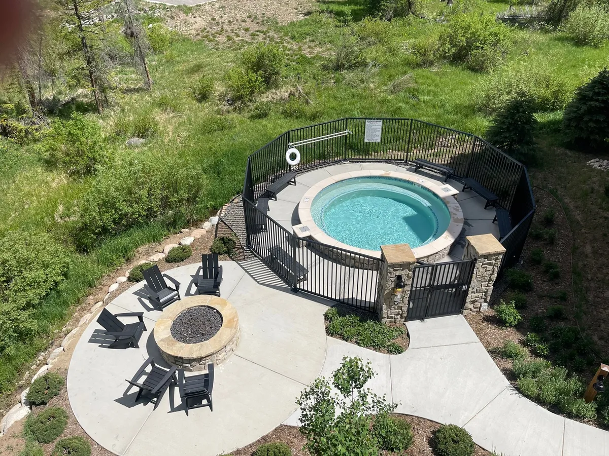 An exterior communal area with a hot tub, fire pit, lounge chairs, and lush greenery. The setting is inviting and encourages socializing or relaxing in a serene mountain environment.